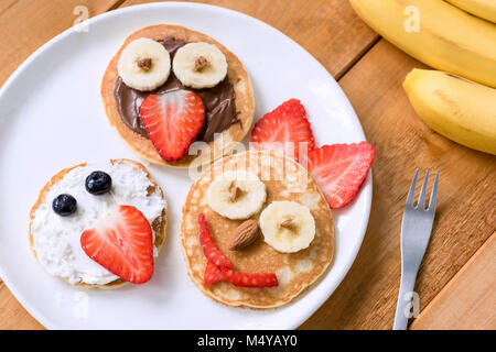 Pfannkuchen mit Lustige Gesichter für Kinder eingerichtet. Gesundes Obst Pfannkuchen für Kinder Essen Stockfoto