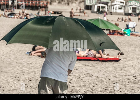Man Walking am Strand unter einem grünen Dach Schutz vor der Sonne Stockfoto