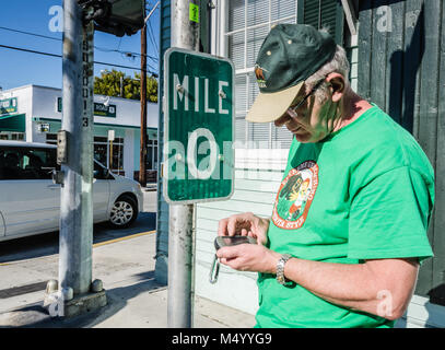 Geocacher prüft GPS am Anfang der US Route 1. US1 entlang der Ostküste von Florida, beginnend in Key West mit 2.369 Meilen (3,81 Stockfoto