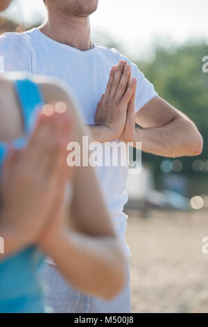 Fitness, Sport, Freundschaft und Lifestyle-Konzept - lächelnde paar machen Meditation Yoga-Übungen am Strand am Morgen Stockfoto