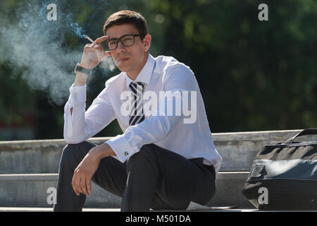 Gut gekleidete Business-Mann Rauchen sitzen auf einer Straße Bürgersteig Stockfoto