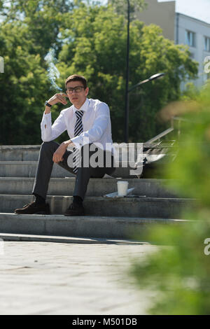 Gut gekleidete Business-Mann Rauchen sitzen auf einer Straße Bürgersteig Stockfoto
