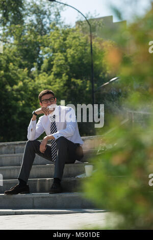 Gut gekleidete Business-Mann Rauchen sitzen auf einer Straße Bürgersteig Stockfoto
