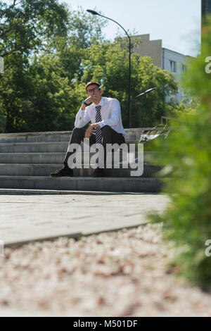 Gut gekleidete Business-Mann Rauchen sitzen auf einer Straße Bürgersteig Stockfoto