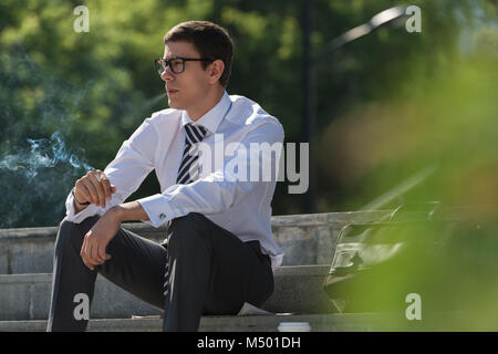 Gut gekleidete Business-Mann Rauchen sitzen auf einer Straße Bürgersteig Stockfoto
