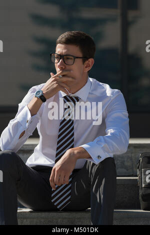 Gut gekleidete Business-Mann Rauchen sitzen auf einer Straße Bürgersteig Stockfoto