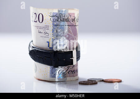 In der Nähe von bis Zwanzig Pfund Währung Anmerkung innerhalb der Armbanduhr auf dem Schreibtisch gerollt Stockfoto