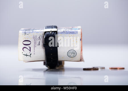 In der Nähe von bis Zwanzig Pfund Währung Anmerkung innerhalb der Armbanduhr auf dem Schreibtisch gerollt Stockfoto