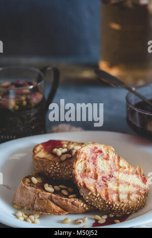 Toast Brot mit Sesamsamen hausgemachte Kuchen mit Pinienkernen auf weiße Platte mit einem Becher der Blütenknospen rot Trocken rose Kaffee und Cherry ja eingerichtet Stapel Stockfoto