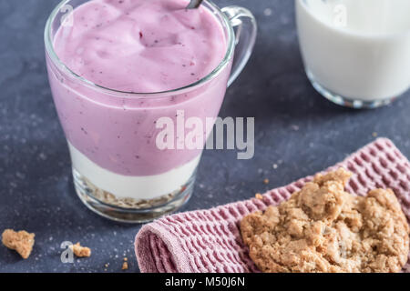 Heidelbeere Joghurt natur Haferflocken Müsli mehrere Schichten aus Glas mit Dekor serviette Handtuch dessert Löffel und Milchkännchen und zerbröckelt gebrochen Cookies auf Stockfoto