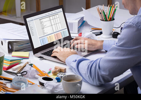 Nahaufnahme der Geschäftsmann mit Laptop über die unordentlichen Schreibtisch am Arbeitsplatz im Büro Stockfoto