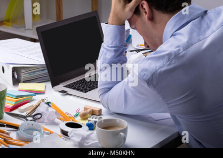 Close-up von stressigen Geschäftsmann mit Laptop auf unordentlichen Schreibtisch am Arbeitsplatz Stockfoto