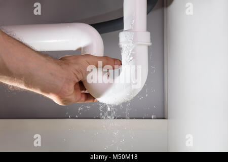 Close-up In eines Mannes Hand, die Leckage weiße Waschbecken Rohr in der Küche Stockfoto