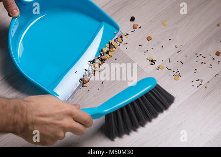 Nahaufnahme der männlichen Fegen Holzboden mit kleinen Handfeger und Kehrblech Stockfoto