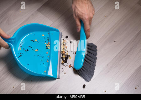 Nahaufnahme der männlichen Fegen Holzboden mit kleinen Handfeger und Kehrblech Stockfoto