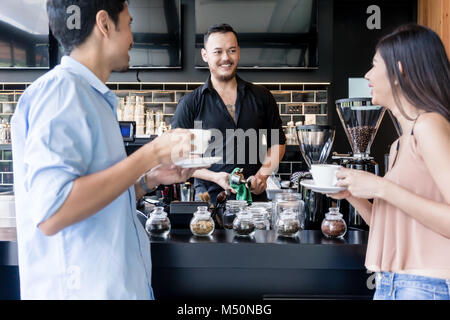 Fröhlicher junger Barkeeper Reinigung der Kaffeemaschine, während im Gespräch Stockfoto