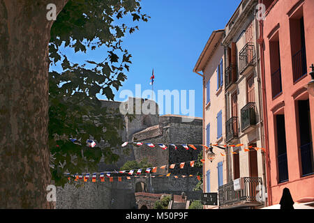 Bunte Straße in Collioure, Pyrénées-Orientales, Royal, Frankreich, mit Chateau-Royal im hinteren und Französischen und Katalanischen nationale Flaggen Stockfoto