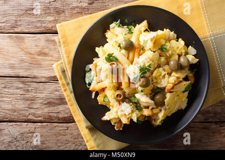 Gebratene geschreddert Kabeljau mit Kartoffeln, Zwiebeln, Ei und Oliven auf einen Teller auf den Tisch closeup. horizontal oben Ansicht von oben Stockfoto