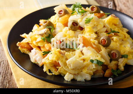 Gebratene Stockfisch mit Kartoffeln, Zwiebeln und ein Omelett auf einer Platte close-up auf einem Tisch. Horizontale Stockfoto