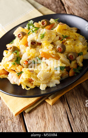 Die schmackhafte portugiesische Küche: Bacalhau Bass Kabeljau mit Kartoffeln, Zwiebeln und Omelett auf einer Platte close-up auf einem Tisch. Vertikale Stockfoto