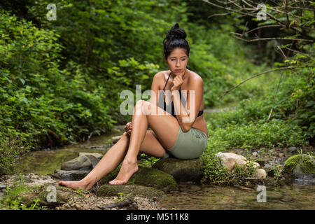 Junge Frau sitzt auf einem Stein im Stream Stockfoto