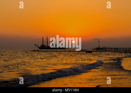 Piratenschiff im Ozean, wunderschönen Sonnenuntergang über dem Ozean, im Meer, Wellen am Strand, rot gefärbt Stockfoto