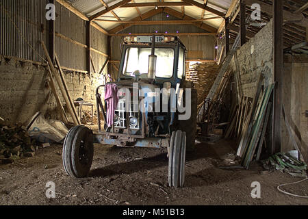 Ein alter Ford Traktor in einer alten Scheune mit dem Morgen Sun Streaming durch die Kabine renoviert. Stockfoto