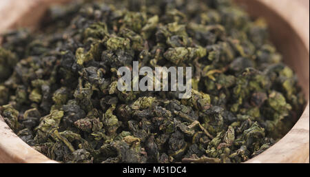 Trocken grüne Tee Blätter fallen in Holz Schüssel auf den Tisch, breiten Foto Stockfoto