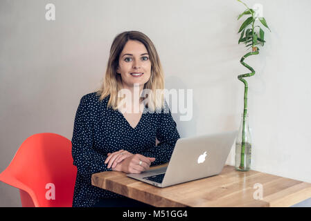 Ein junger Junge Frau schreibt ein blog aus einem Café in eine alternative und moderne Art zu Arbeiten auf Ihrem Laptop beim Trinken einen Kaffee Stockfoto