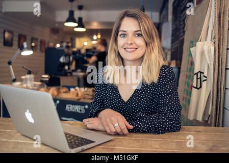 Ein junger Junge Frau schreibt ein blog aus einem Café in eine alternative und moderne Art zu Arbeiten auf Ihrem Laptop beim Trinken einen Kaffee Stockfoto