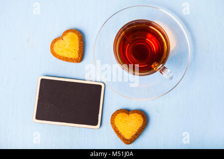 Herzförmige Kekse und Tee auf einem hölzernen Hintergrund. Für Text platzieren. Romantisches Frühstück. Grußkarte für Valentinstag. Stockfoto