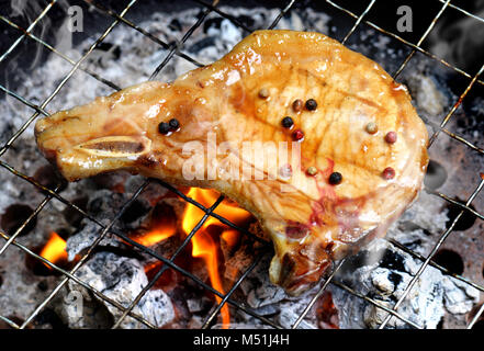 Schweinekoteletts steak Holzkohle Grill Feuer auf BBQ-Soße mit Außenbeleuchtung und Flash Beleuchtung hinzufügen. Stockfoto