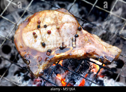 Schweinekoteletts steak Holzkohle Grill Feuer auf BBQ-Soße mit Außenbeleuchtung und Flash Beleuchtung hinzufügen. Stockfoto