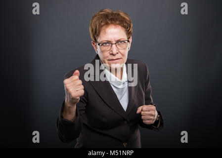 Business ältere Dame holding Fäuste wie Kämpfe auf schwarzem Hintergrund Stockfoto