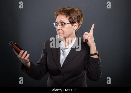 Business ältere Dame in Idee holding Smartphone auf schwarzen Hintergrund mit Copyspace Werbefläche Stockfoto