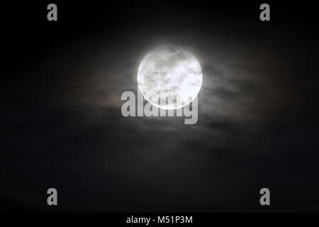 Große silberne leuchtende Mond close-up auf dunklen blauen Himmel mit vereinzelten Wolken. Stockfoto