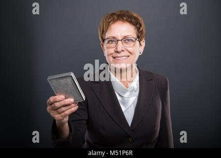 Business ältere Dame holding Zigarettenschachtel und lächelnd auf schwarzem Hintergrund Stockfoto
