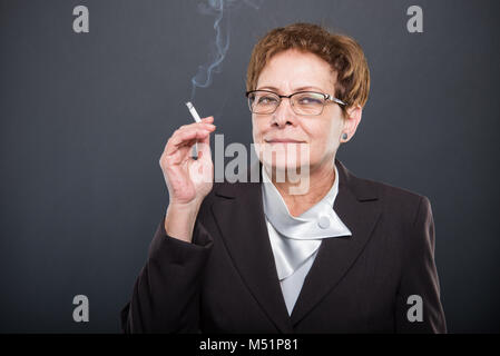 Business ältere Dame genießen Rauchen cigarrete auf schwarzen Hintergrund mit Copyspace Werbefläche Stockfoto