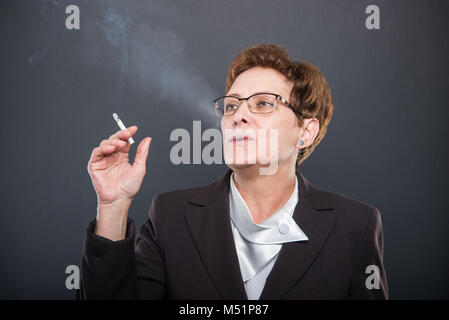 Business ältere Dame genießen Rauchen cigarrete auf schwarzem Hintergrund Stockfoto