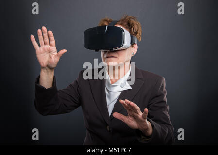 Business ältere Dame tragen VR-Brille und gestikulierend auf schwarzem Hintergrund Stockfoto