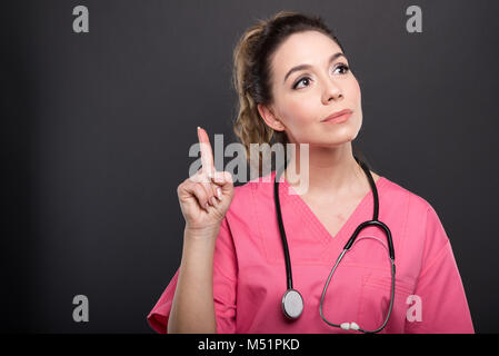 Portrait von attraktiven Dame Arzt holding Finger wie in Idee auf schwarzen Hintergrund mit copypsace Werbefläche Stockfoto