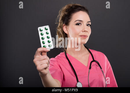 Portrait von schönen jungen Arzt halten zwei Blistern von Pillen auf schwarzen Hintergrund mit copypsace Werbefläche Stockfoto