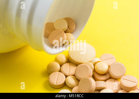 Haufen sortierte beige Kapseln auf gelben Hintergrund. Die Pillen sind sppiling aus der Flasche. Stockfoto