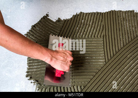 Arbeitnehmer mit Kelle Werkzeug für Fliesen Installation, Mörtel Kleber auf dem Boden Stockfoto