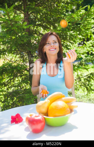 Glücklich lächelnde junge Frau Jonglieren Orangen an Ihrem Garten Stockfoto