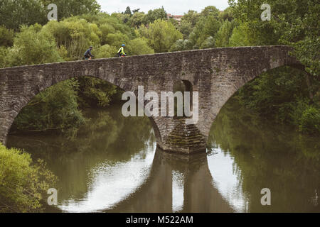 Zwei Radfahrer radeln über alte Bogen Brücke über den Fluss, Pamplona, Navarra, Spanien Stockfoto