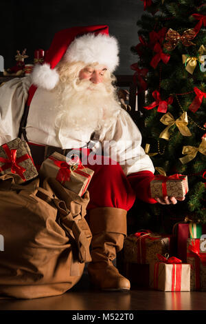 Santa, Geschenke unter dem Weihnachtsbaum im dunklen Zimmer Stockfoto