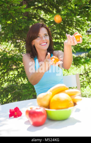 Glücklich lächelnde junge Frau Jonglieren Orangen an Ihrem Garten Stockfoto