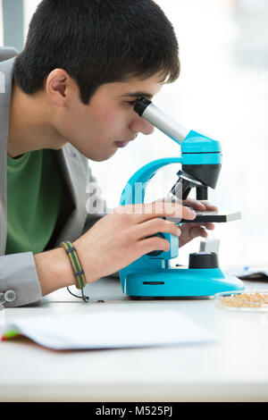 High School Schüler. Jungen gutaussehenden männlichen Kursteilnehmer blickt durch Mikroskop in Wissenschaft Klassenzimmer Stockfoto