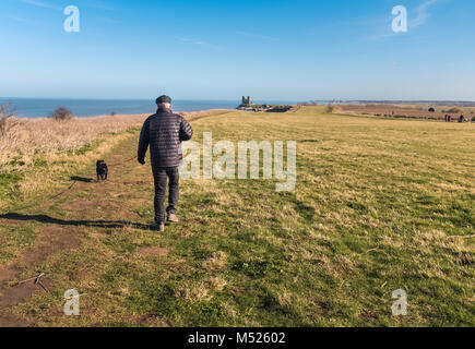 Ein Mann, der seinen Hund an Reculver Towers, Reculver, Kent, Großbritannien entlang der Klippe Spaziergang auf dem Küstenweg in der Nähe von Herne Bay und Whitstable. Stockfoto